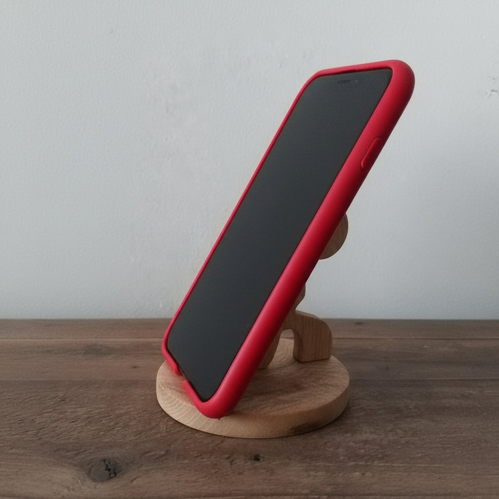 A red protective phone case on a smartphone, displayed on a small wooden stand on a wooden tabletop against a light gray wall.