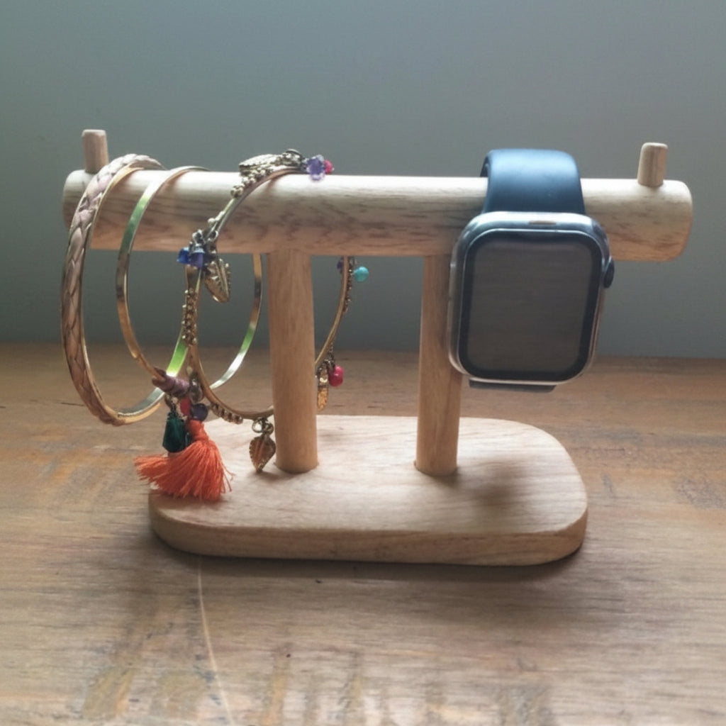 A light natural wood jewelry organizer stand holding several bracelets and a smartwatch, placed on a wooden tabletop against a soft gray wall.