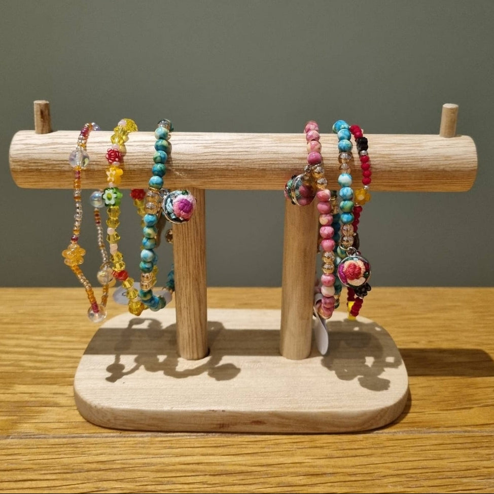A set of colorful beaded bracelets displayed on a small wooden jewelry stand, placed on a wooden tabletop against a plain gray wall.